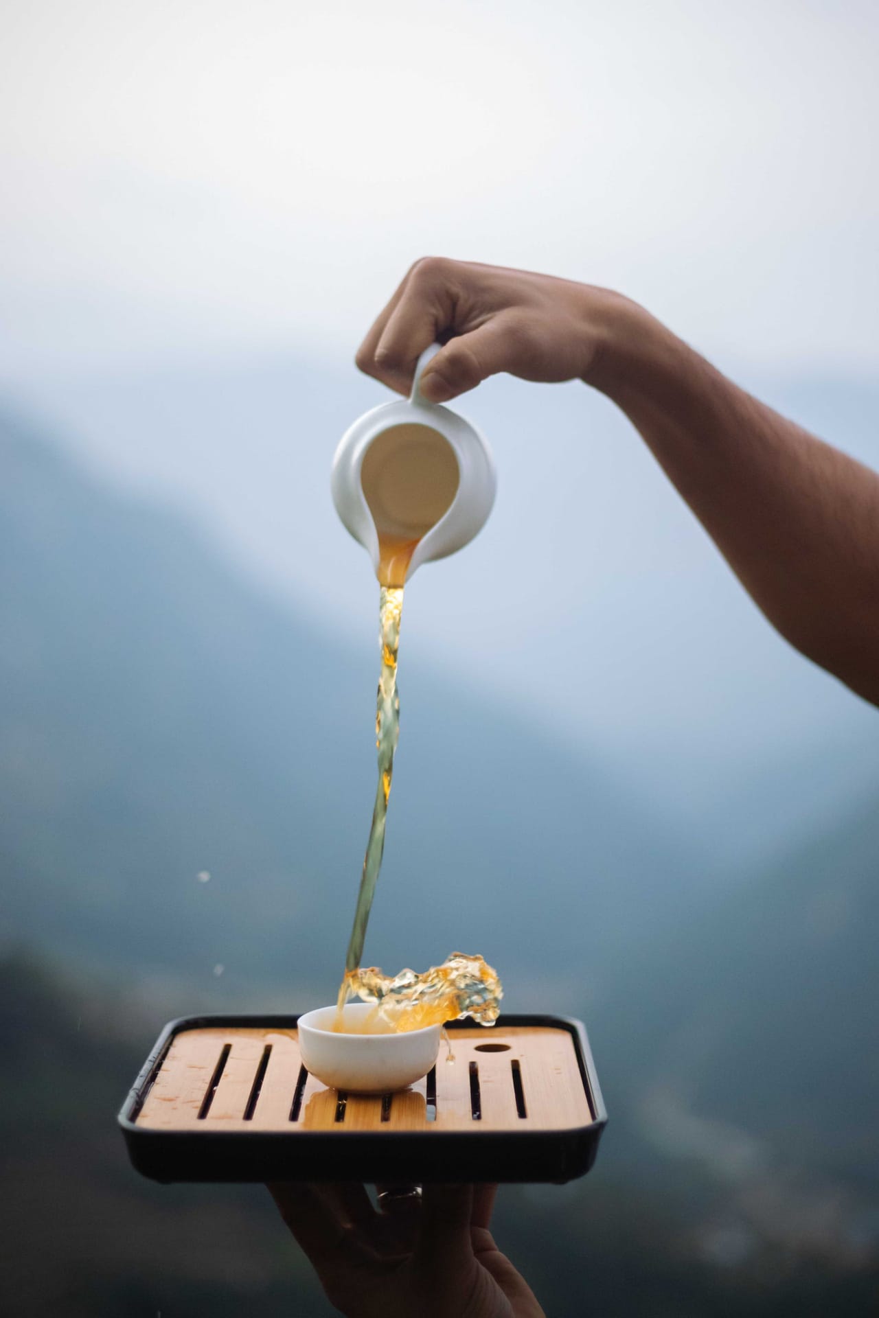 Tea poured slowly into a cup on a wooden tray