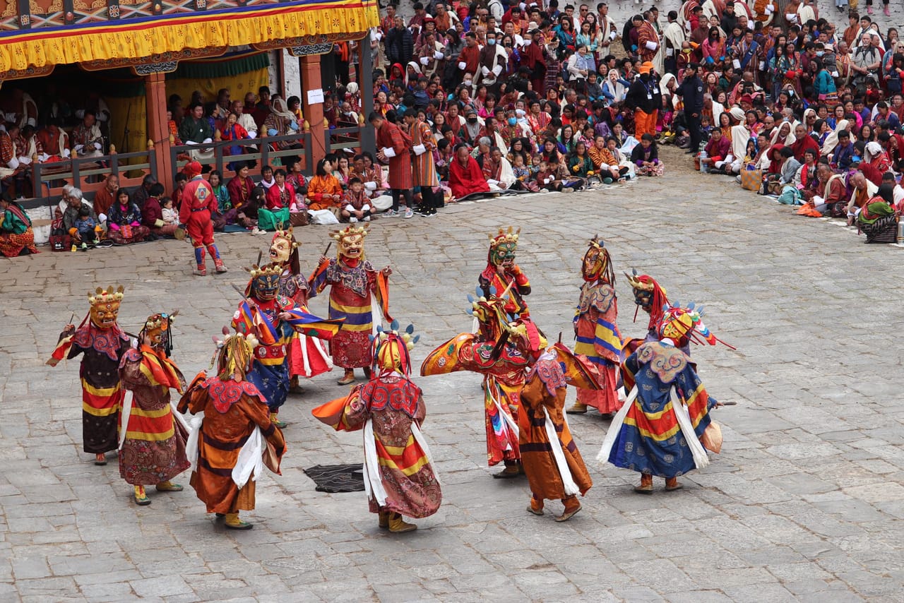 Masked tshechu dancers mid-turn, robes flaring