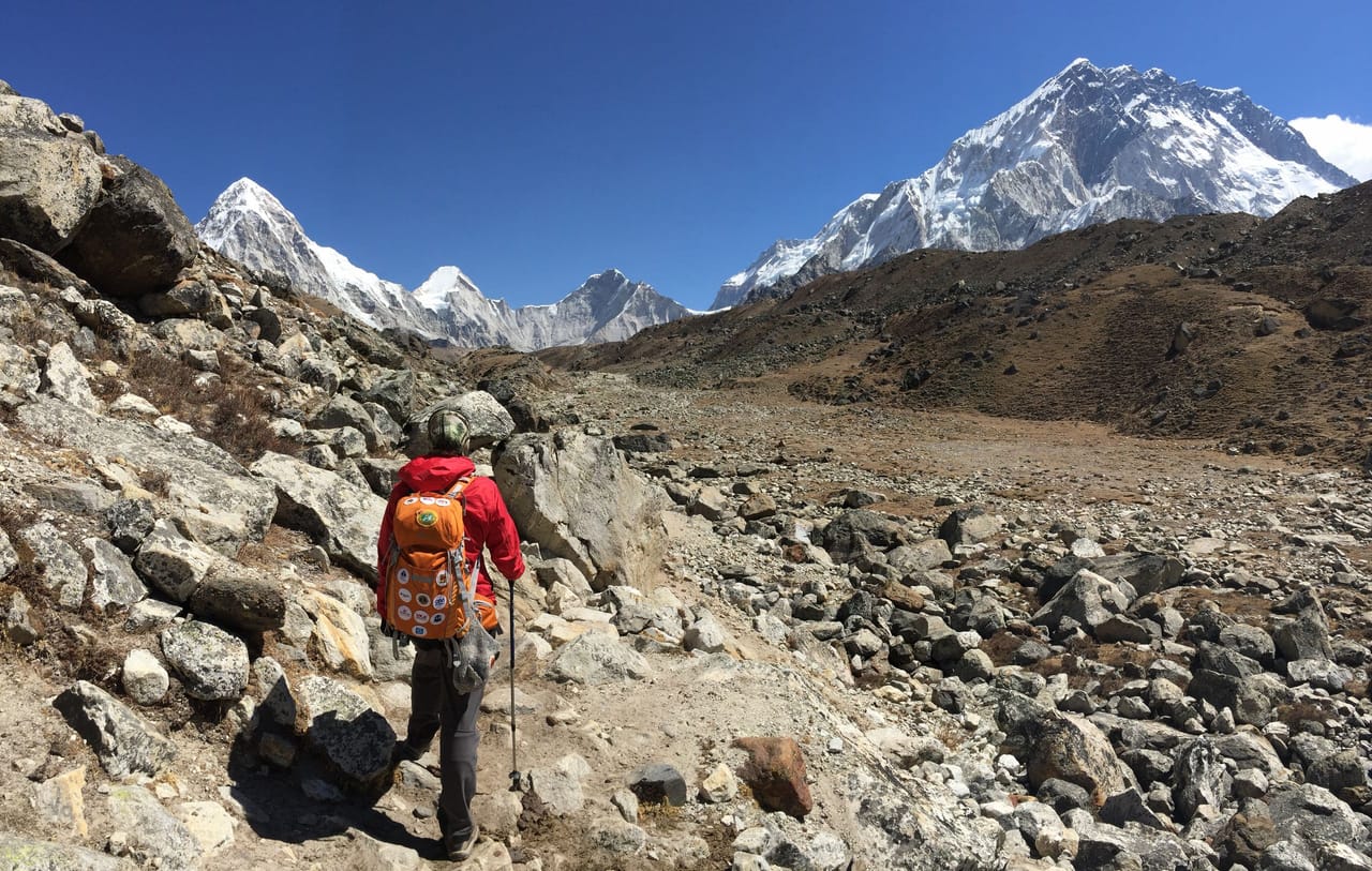 A trekker on a Himalayan trail below snow-capped peaks