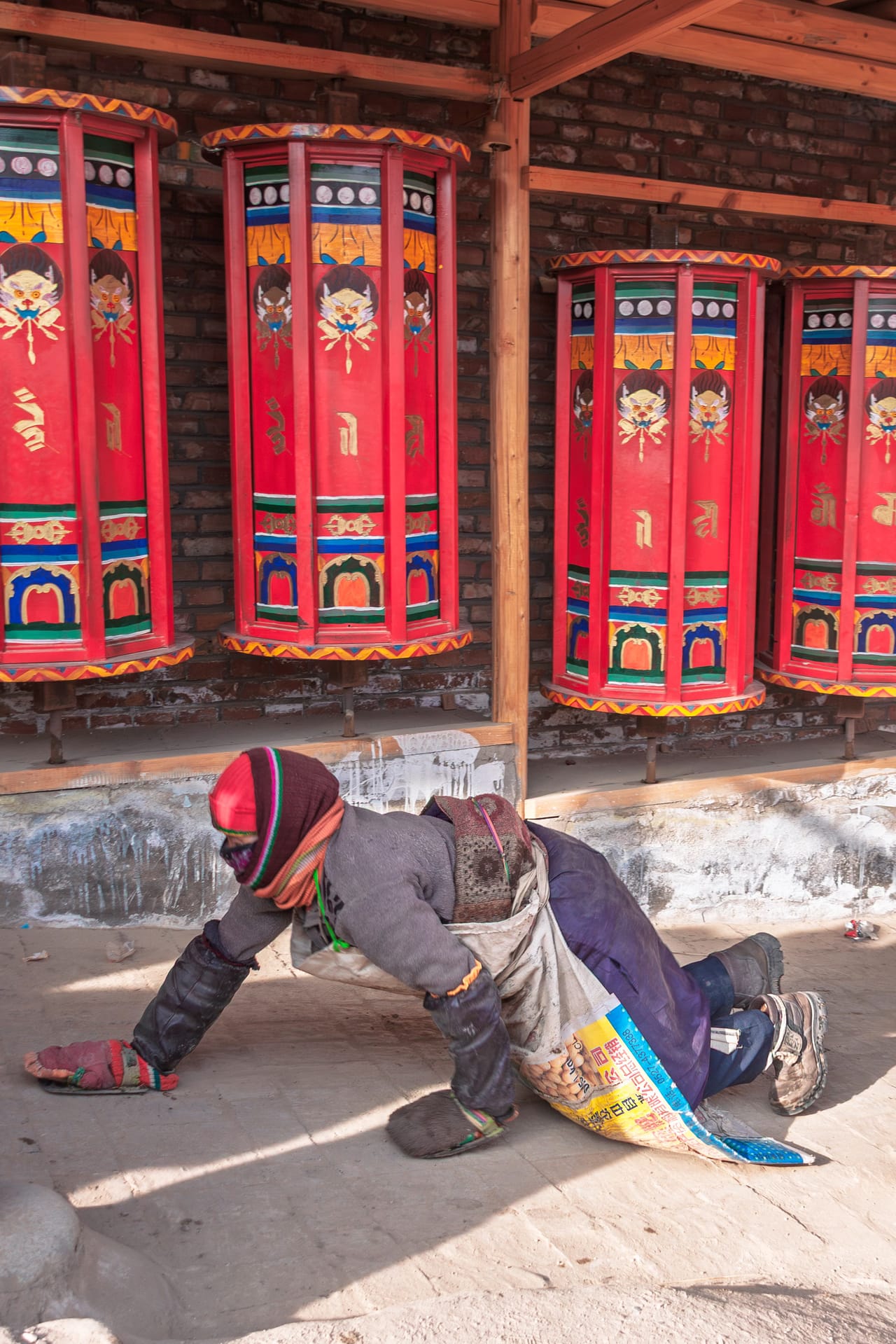 A pilgrim prostrating past a wall of prayer wheels