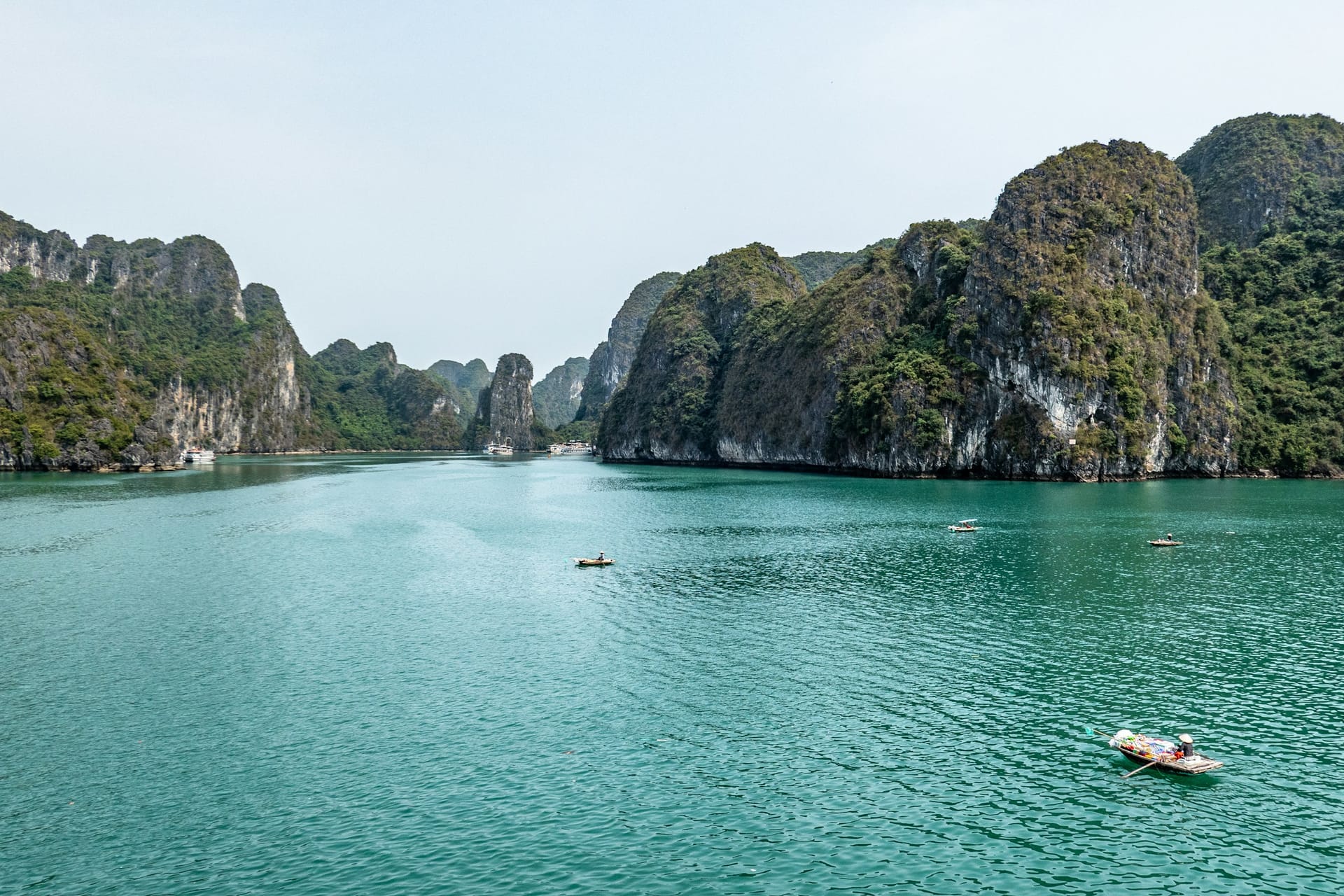 A rowing boat crossing the green water between the karsts of Ha Long Bay